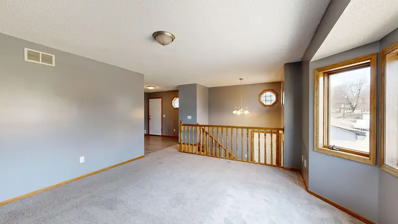 A bright, staged open-plan living area with large windows and a staircase, photographed for a listing