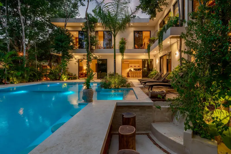 A modern luxury home at dusk with a lit swimming pool and landscaped garden