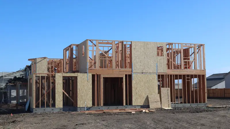 A new home in the framing stage on a suburban lot under a clear sky